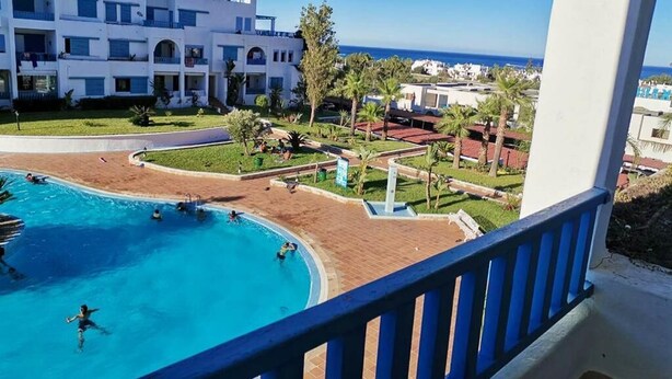 Un albergo con piscina, palme e vista mare.