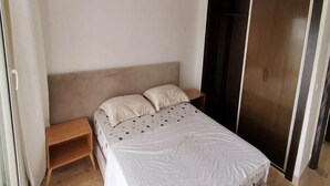 Um quarto com uma cama, mesa de cabeceira, guarda-roupa e um pequeno banco de madeira.