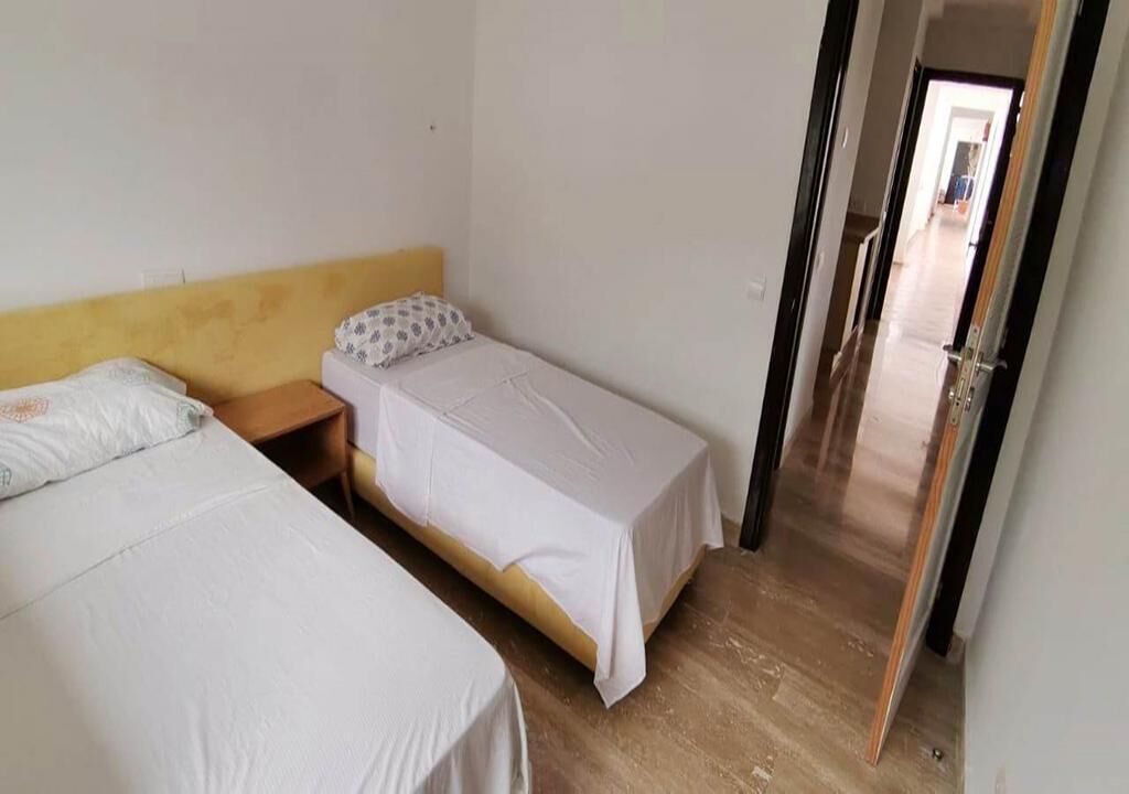 A small, clean room with two single beds, a wooden headboard, and a door leading to another room.