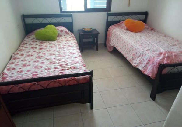 Una habitación con dos camas individuales, cada una con un cojín diferente, una mesita y una ventana.