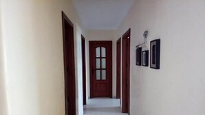 A hallway with a wooden door at the end, white walls, and a tiled floor. - Residence Kabila Vista 4941 (Mdiq)