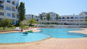 A swimming pool with a tiled deck, surrounded by lounge chairs and a building with multiple balconies in the background. - Residence Kabila Vista 4941 (Mdiq)