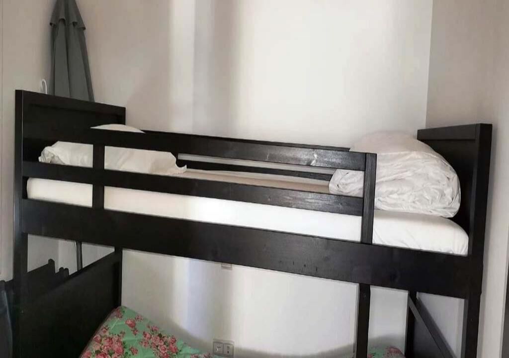 A bunk bed with white bedding and a green floral bedspread at the bottom bunk.
