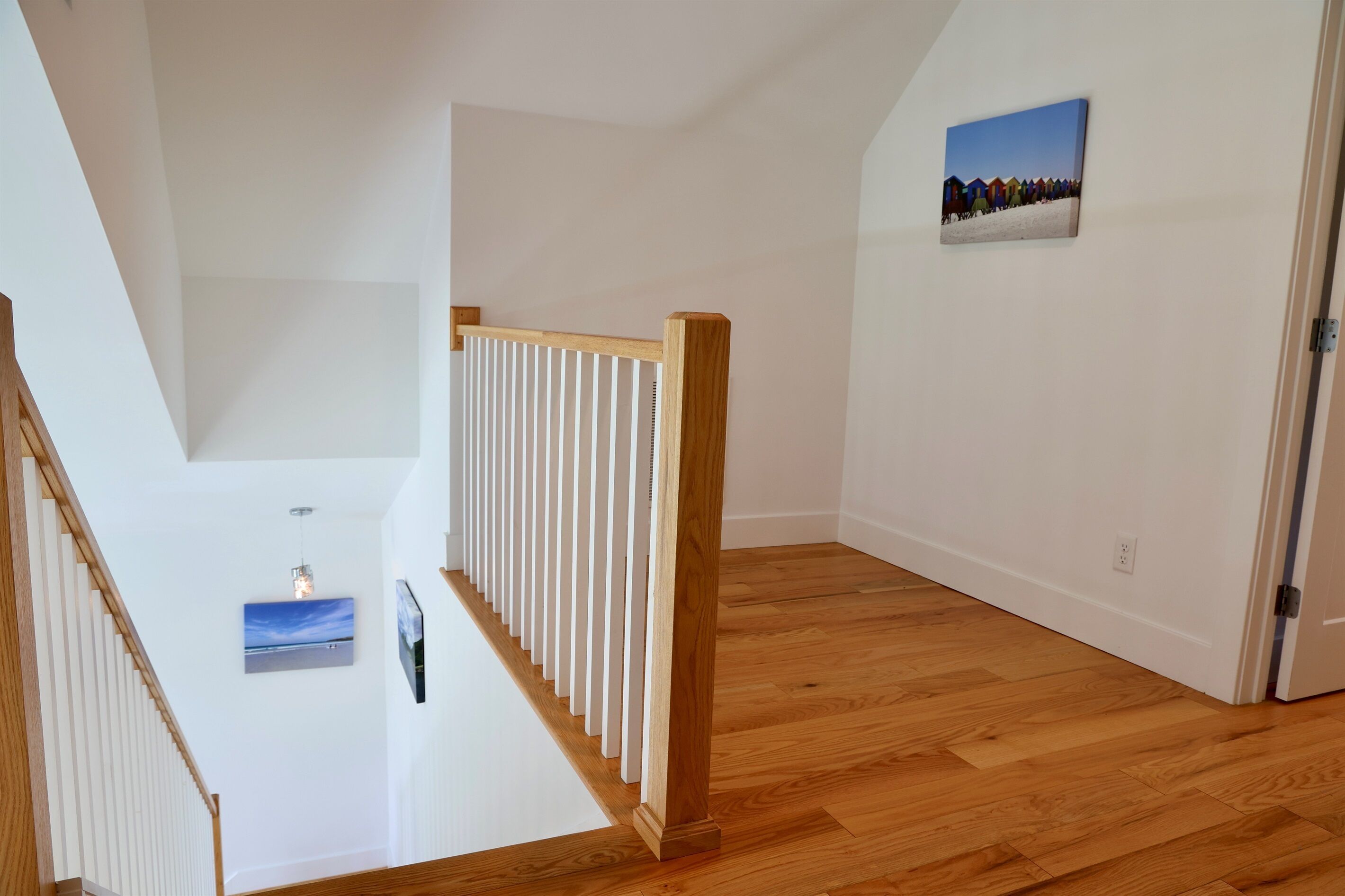 Een trap met houten leuningen, een witte muur met een schilderij en een houten vloer.