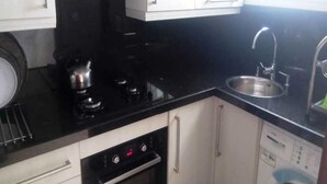 Una cocina con encimera negra, pileta de acero inoxidable y alacenas blancas.