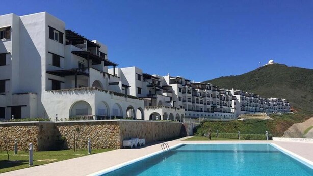 Una piscina con un muro de piedra y un edificio al fondo con múltiples balcones y arcos.