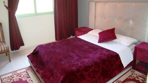 Quarto com uma cama grande, cabeceira, mesa de cabeceira, cadeira e janela com cortinas.
