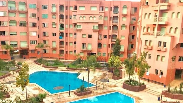 Um hotel com vários andares e um pátio central com duas piscinas, rodeado por vegetação e palmeiras.