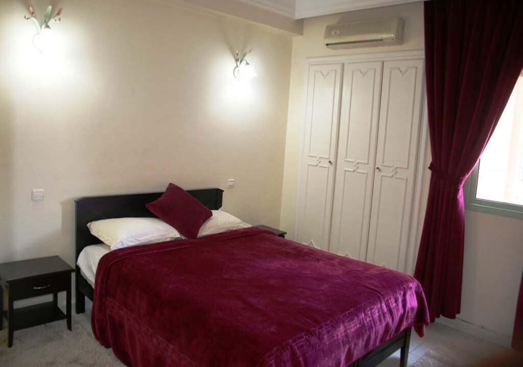 A bedroom with a bed, a nightstand, a wardrobe, and a window with curtains.