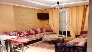 A living room with a sofa, a small table, a TV mounted on the wall, and a window with curtains. - Holiday residence Islane Agadir 4981 (Agadir)