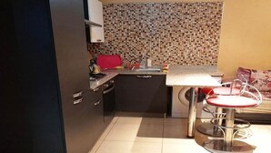 A compact kitchen with a tiled backsplash, a small dining area with a red chair, and a black cabinet. - Holiday residence Islane Agadir 4981 (Agadir)