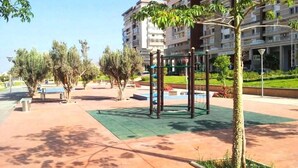 Un espace extérieur comprenant une aire de jeux, des bancs et des arbres.