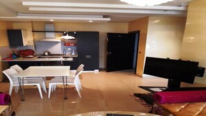 Un salon moderne avec un coin repas, une cuisine à l’arrière-plan et un téléviseur à écran plat posé sur un meuble.
