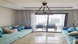Ein geräumiges Wohnzimmer mit einer großen Sofagarnitur, einem Kronleuchter und Blick durch eine Glastür auf einen Außenbereich.
