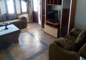 A living room with a sofa, a coffee table, a TV on a wooden stand, and patterned rugs.