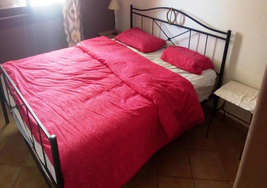 A bed with a metal frame, a red bedspread, and two pillows.
