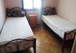 Une petite chambre avec deux lits simples, une table de chevet en bois et une fenêtre.