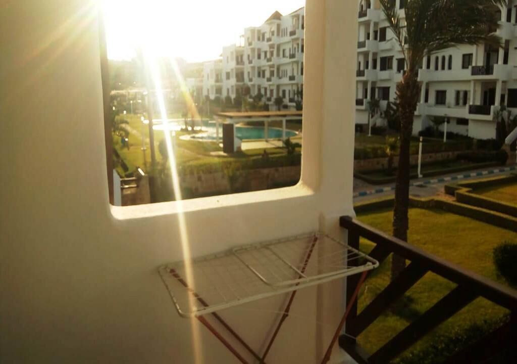 Un balcón con un tendedero, vistas a una piscina y edificios de apartamentos.