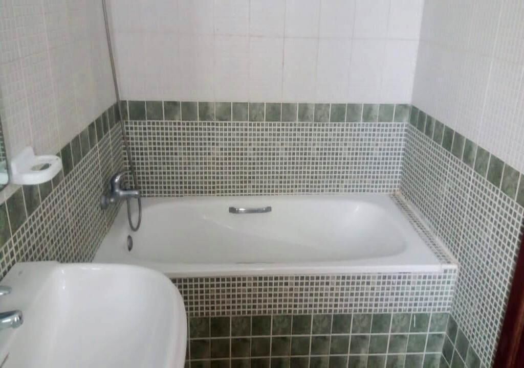 Une salle de bain avec une baignoire blanche, un lavabo et des murs recouverts de carreaux verts.