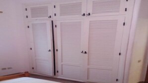 Un dormitorio con una cama grande, un armario blanco con puertas batientes y suelo de baldosas.