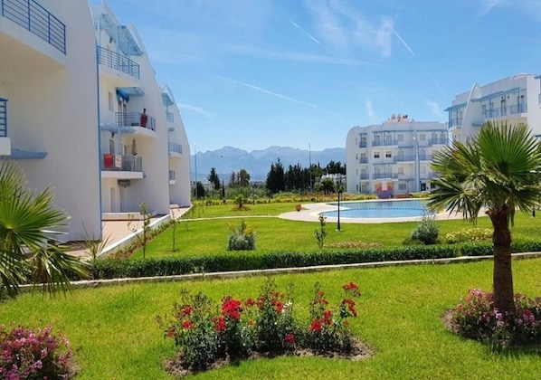 A modern hotel with a pool, well-maintained gardens, and a clear view of mountains in the background.