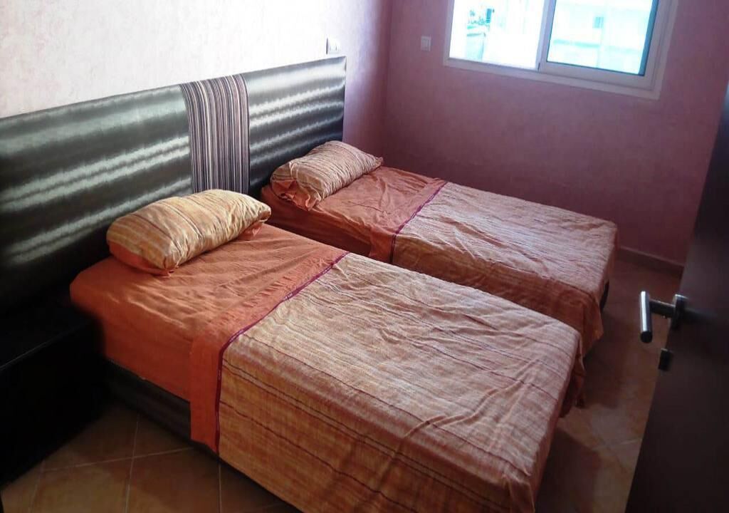 Quarto com duas camas, cada uma com cabeceira listrada e roupa de cama laranja.