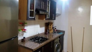 A kitchen with dark wooden cabinets, a stainless steel refrigerator, a gas stove, and a washing machine. - Residence Riviera Beach 5024 (Cabo Negro)