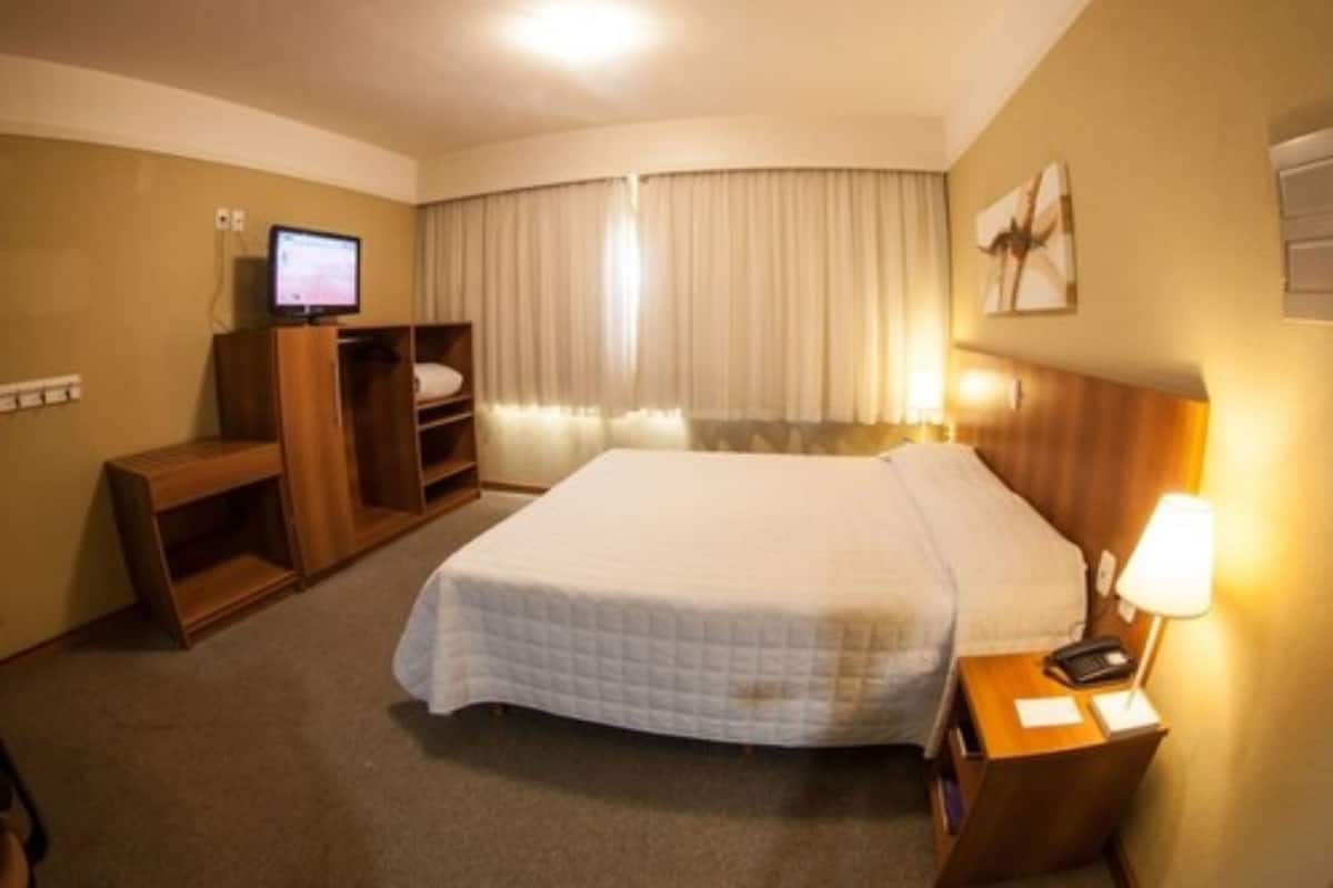 Una habitación de hotel con una cama, un escritorio con una computadora, un televisor y una lámpara.