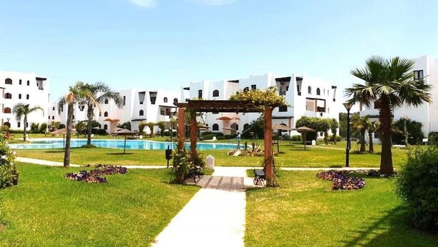 A hotel courtyard with a pool, a pergola, and palm trees.