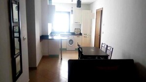 A compact kitchen with a washing machine, a dining area with a table and chairs, and a visible door leading to another room.