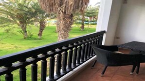 Un balcon doté d’une balustrade noire, d’une chaise en osier et offrant une vue sur une pelouse verdoyante bordée de palmiers.