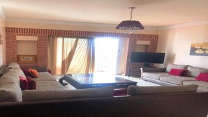 Ein Wohnzimmer mit einer Sofagarnitur, einem Couchtisch, einem Flachbildfernseher und einer Deckenleuchte.
