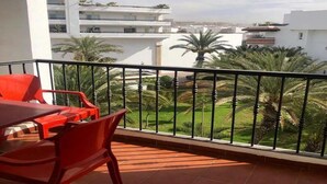 Ein Balkon mit roten Stühlen und einem Tisch, der auf einen Garten mit Palmen und einen Blick auf andere Gebäude blickt.