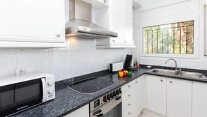 A modern kitchen with white cabinets, a built-in microwave, a stove, and a window with a view of greenery. - Can Berta by Interhome (Pals)