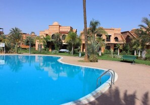 A swimming pool with a curved edge, surrounded by palm trees and a building with a dome-shaped roof. - Residenz Atlas Golf Resort 5098 (Marrakech)