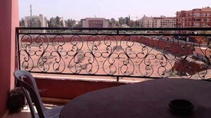 Un balcon doté d’une balustrade en fer forgé, donnant sur une cour intérieure avec des bâtiments en arrière-plan.
