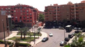 Un immeuble résidentiel à plusieurs étages, doté de balcons, d’un espace de stationnement et d’un petit espace paysager agrémenté de palmiers.