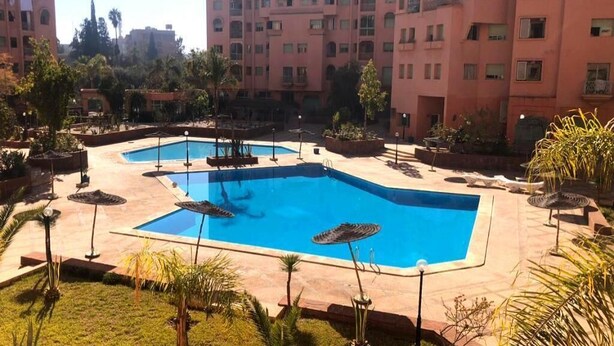 Une cour dotée de deux piscines, entourée de palmiers et bordée d’un immeuble à plusieurs étages avec des balcons.