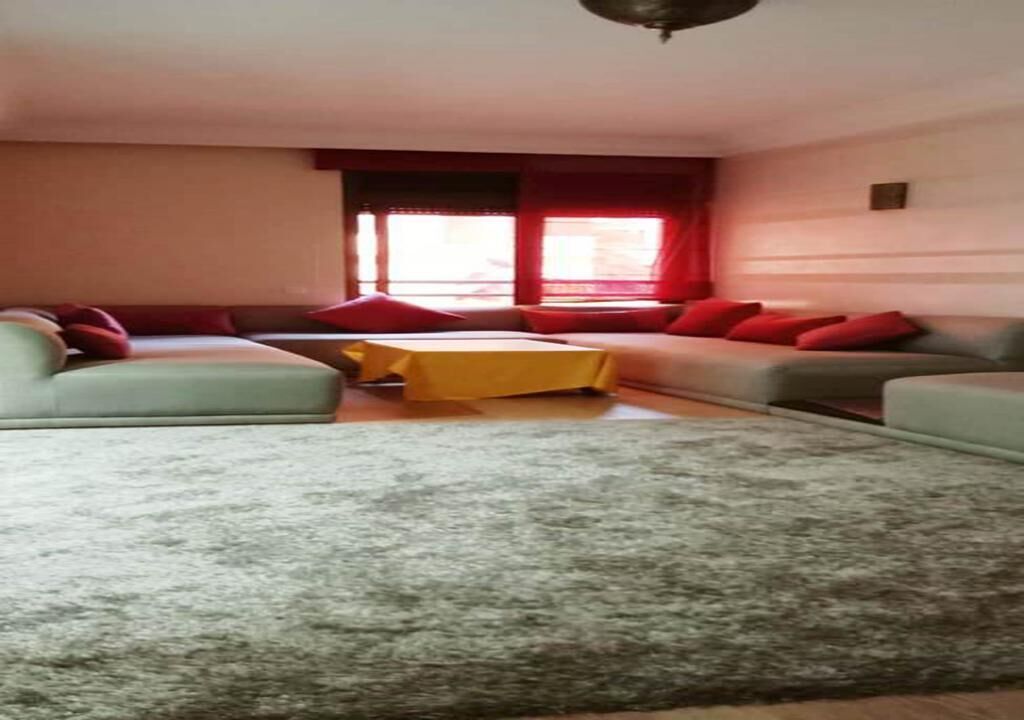 Ein Wohnzimmer mit grauem Teppich, zwei Sofas mit roten Kissen, einem gelben Couchtisch und einem Fenster mit roten Vorhängen.