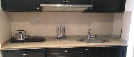 A compact kitchen with dark cabinets, a stainless steel sink, and a small refrigerator.