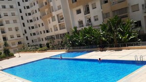 En swimmingpool med ett kaklat poolområde, omgiven av en byggnad med flera våningar och balkonger.
