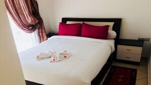 A neatly made bed with white bedding and red pillows, a bedside table with a lamp, and a red rug on the floor.