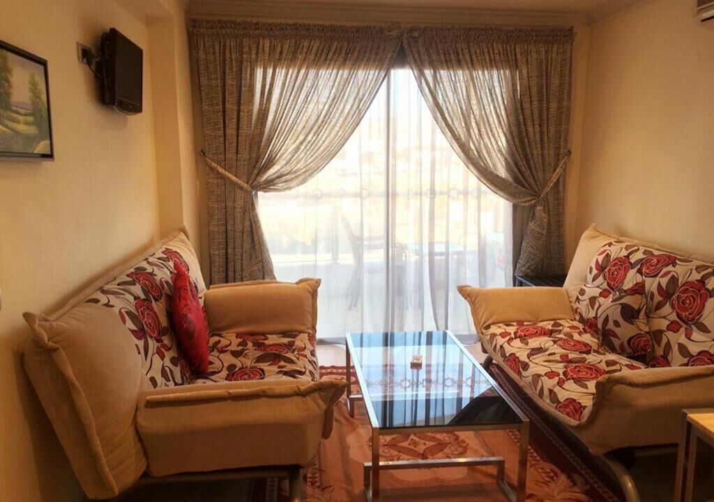 Ein Wohnzimmer mit zwei Sofas, einem Glastisch und einem an der Wand befestigten Fernseher.