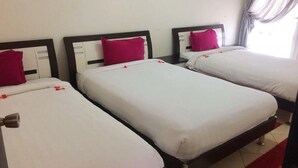 Tres camas individuales con sábanas blancas y almohadas rosas, dispuestas en fila con un cabecero de madera y un tapete rojo decorativo.