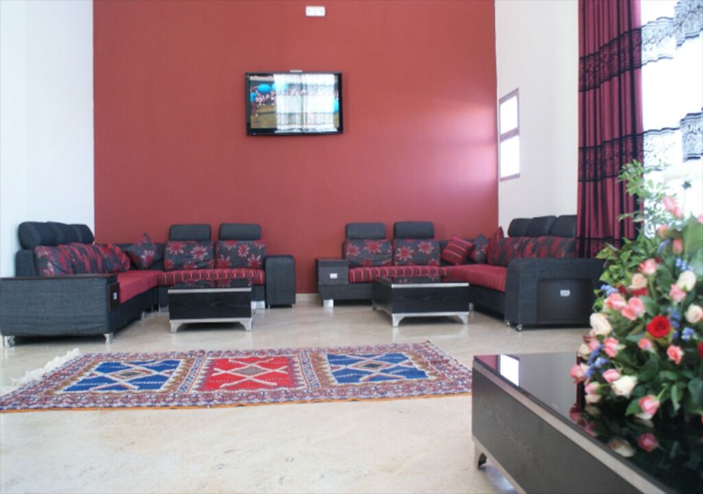 Un hall d’entrée avec un mur rouge, un téléviseur à écran plat fixé au-dessus d’un canapé et un tapis à motifs sur le sol.