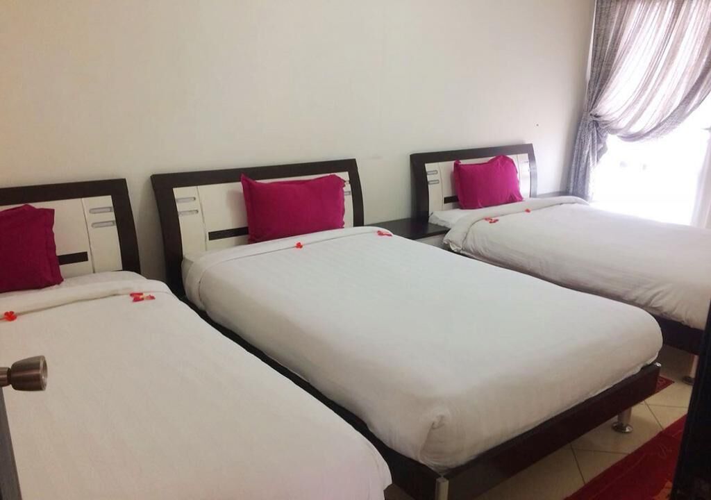 Three single beds with white linens and pink pillows, arranged in a row with a wooden headboard and a red accent rug.