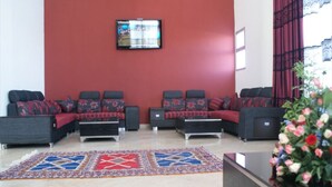 A lobby with a red wall, a flat-screen TV mounted above a sofa set, and a patterned rug on the floor. - Residence Appart Hotel Founty Beach 5142 (Agadir)