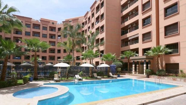 Un albergo con piscina, palme e lettini.