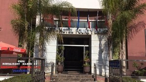 La entrada del Hotel Founty Beach, con escalones que conducen a la puerta, rodeada de palmeras y plantas en macetas.