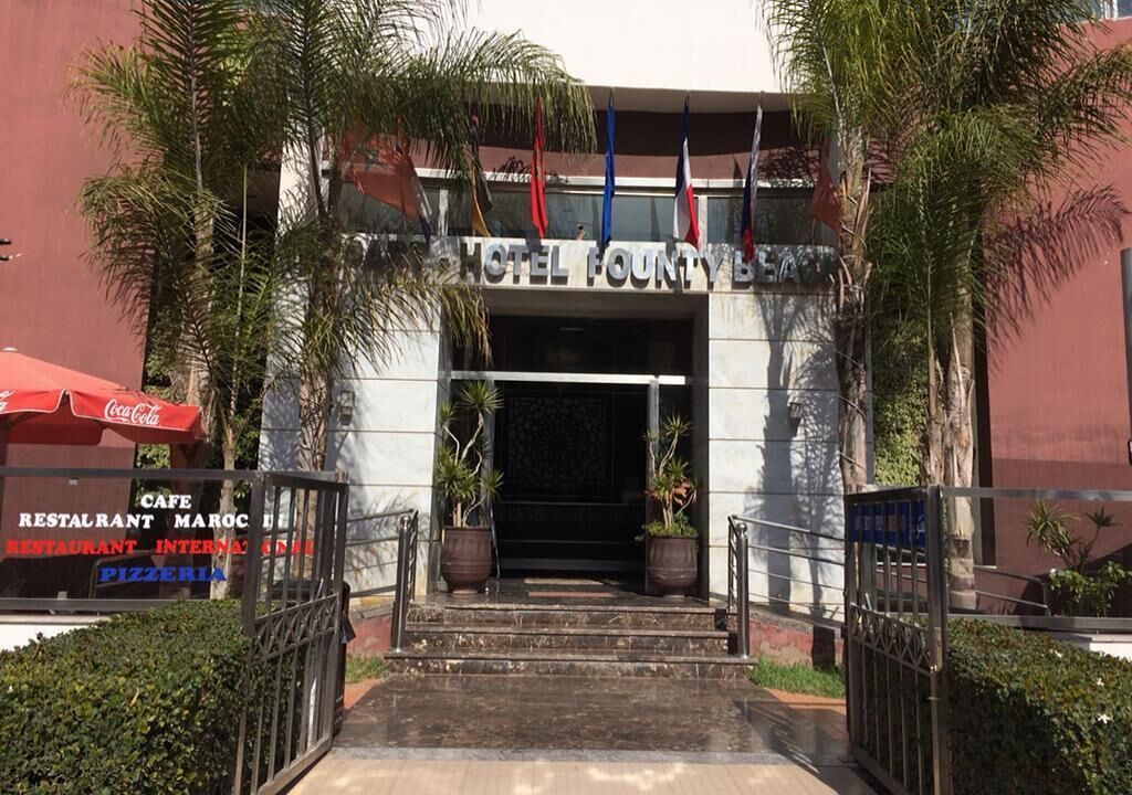 The entrance to Hotel Founty Beach with steps leading up to the door, surrounded by palm trees and potted plants.